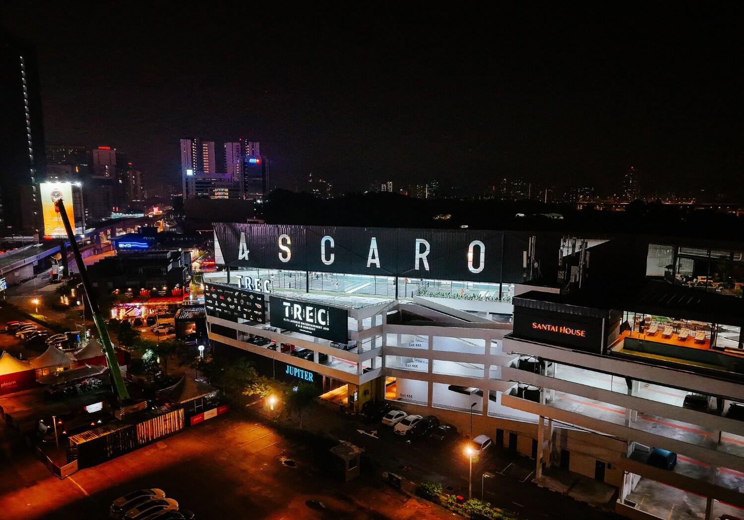 Night view of Ascaro Padel & Social Club building with illuminated signage and surrounding city lights