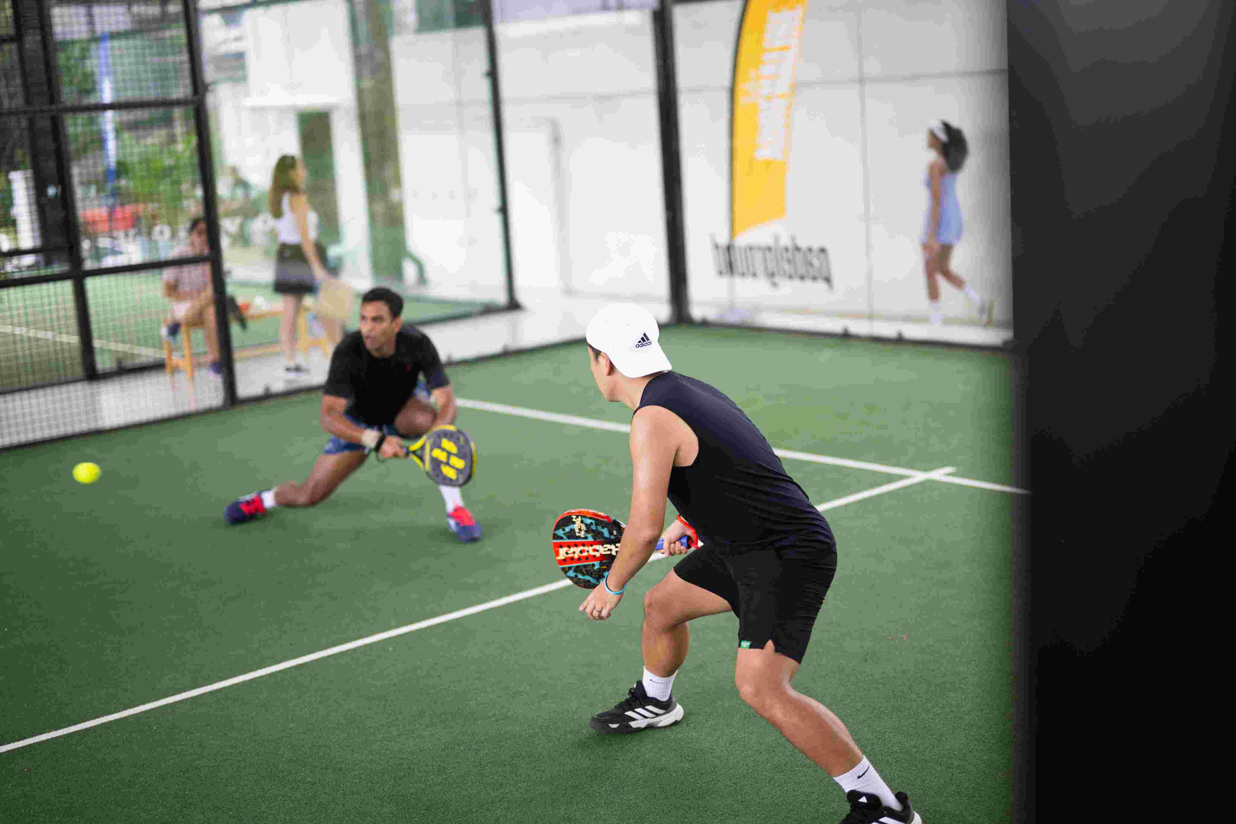 Two padel players holding padel rackets preparing to return a shot on an indoor court.