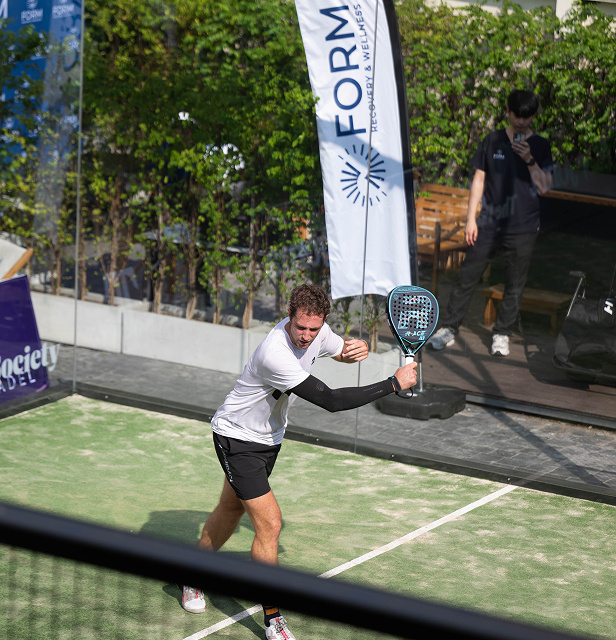 A padel player in a white shirt prepares to hit a shot on an outdoor court.
