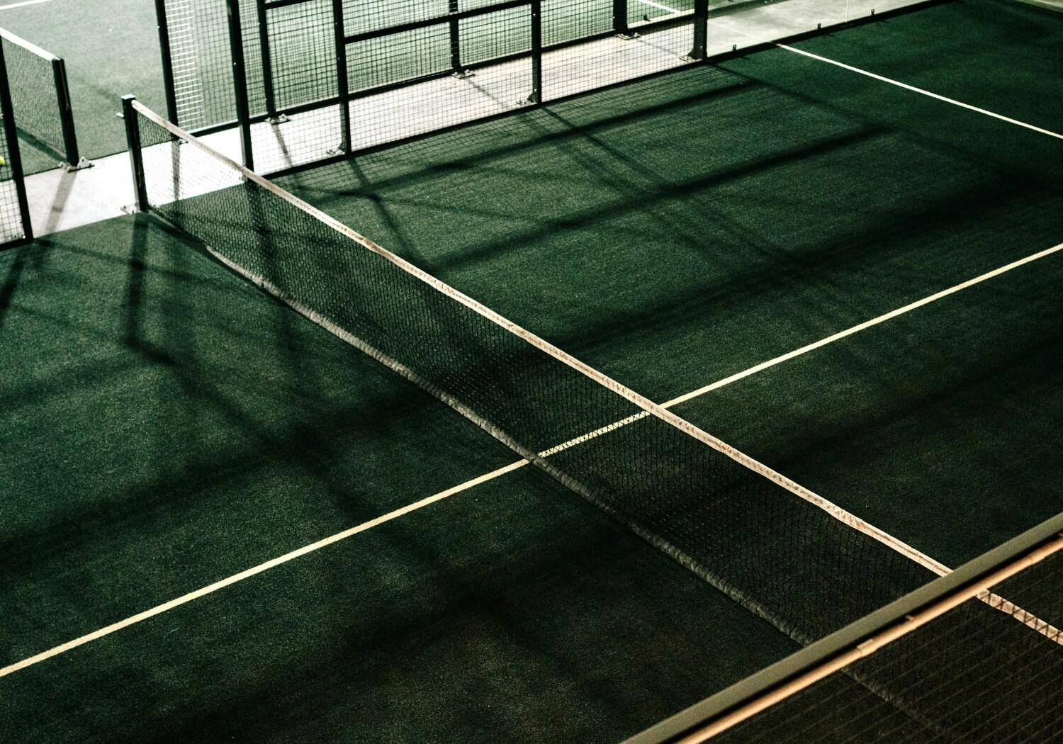 Empty green padel court at The Rally Padel Club with net centred and shadows stretching across the surface