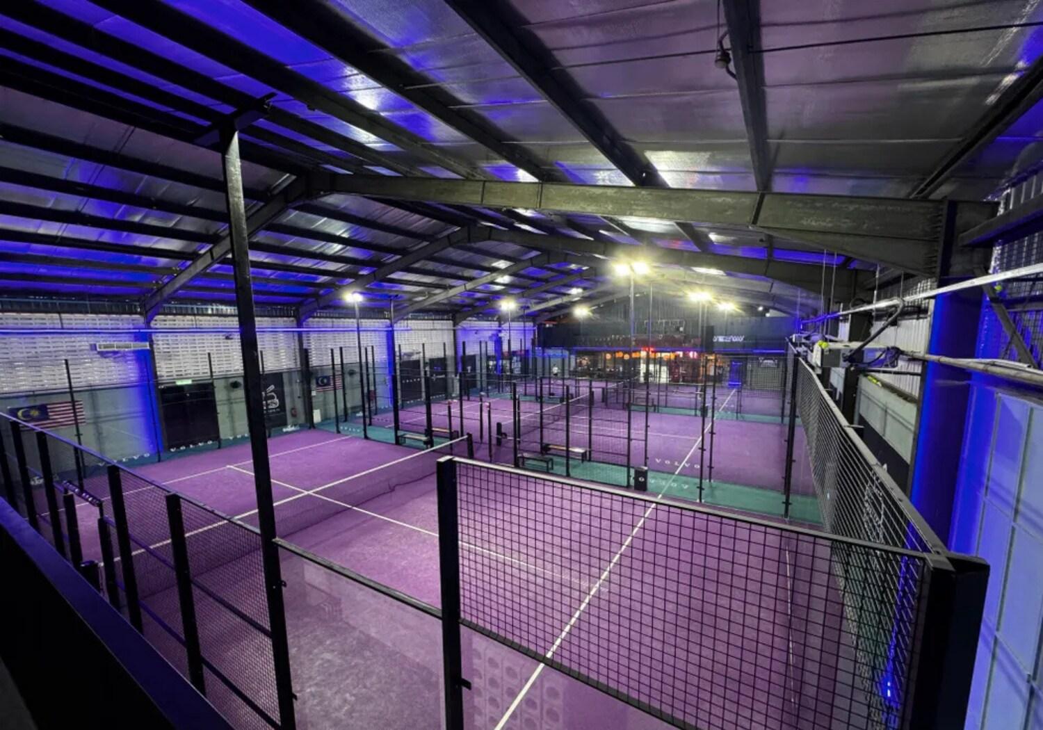 Indoor padel courts at Joy Division Padel featuring purple surfaces and ambient lighting inside a covered facility