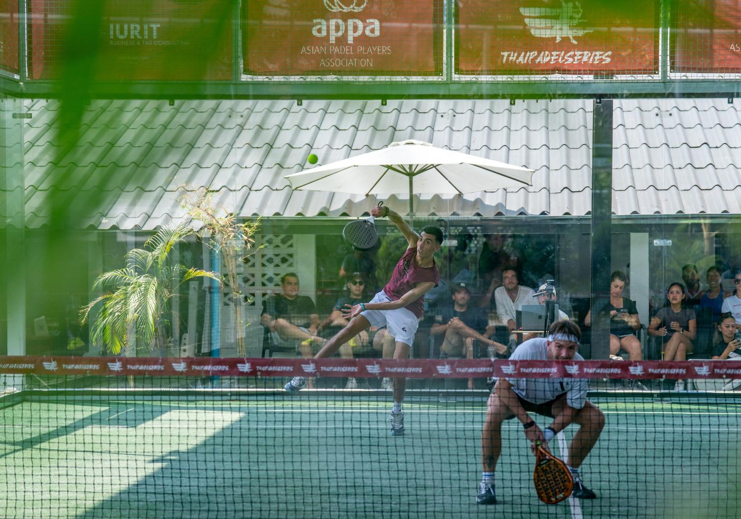 Outdoor padel court at Kross Padel On Nut in Bangkok, Thailand, with palm trees and a swimming pool in the background