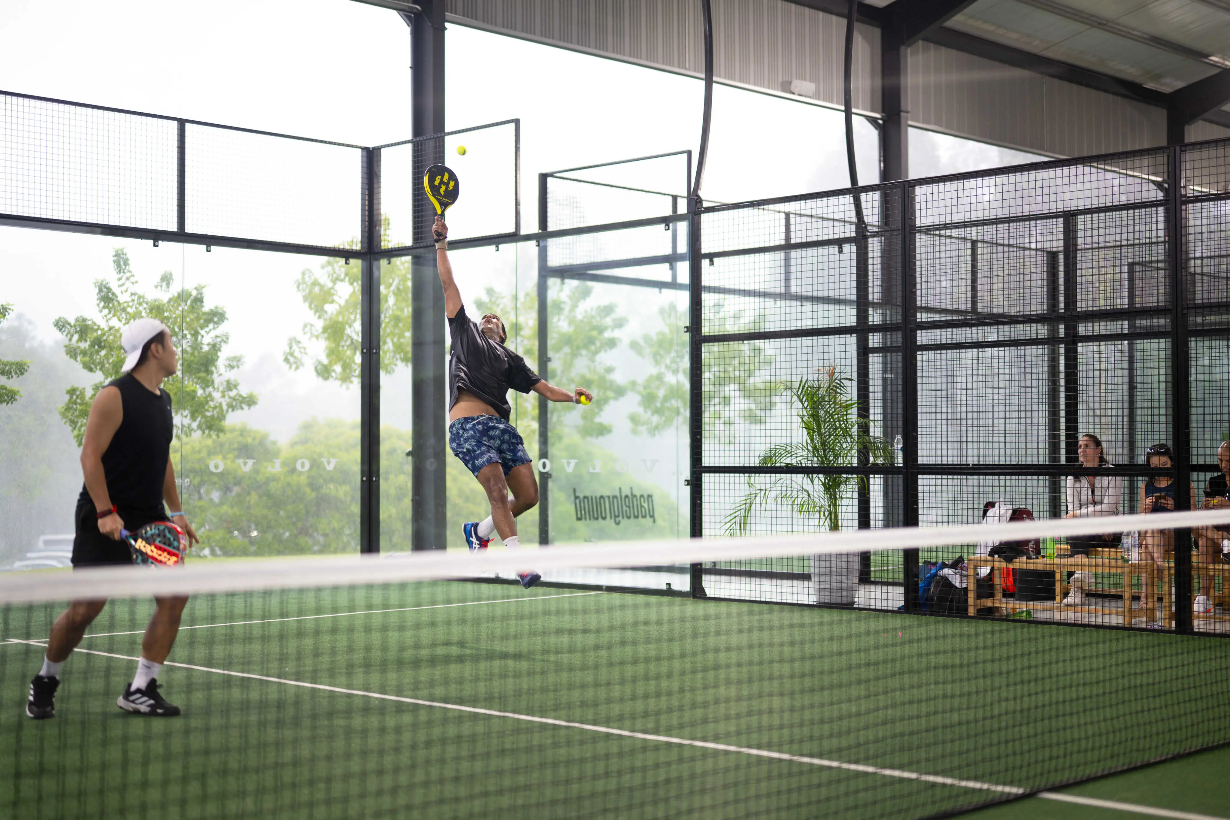 Padel player airborne, executing a powerful smash during a match on an indoor court.