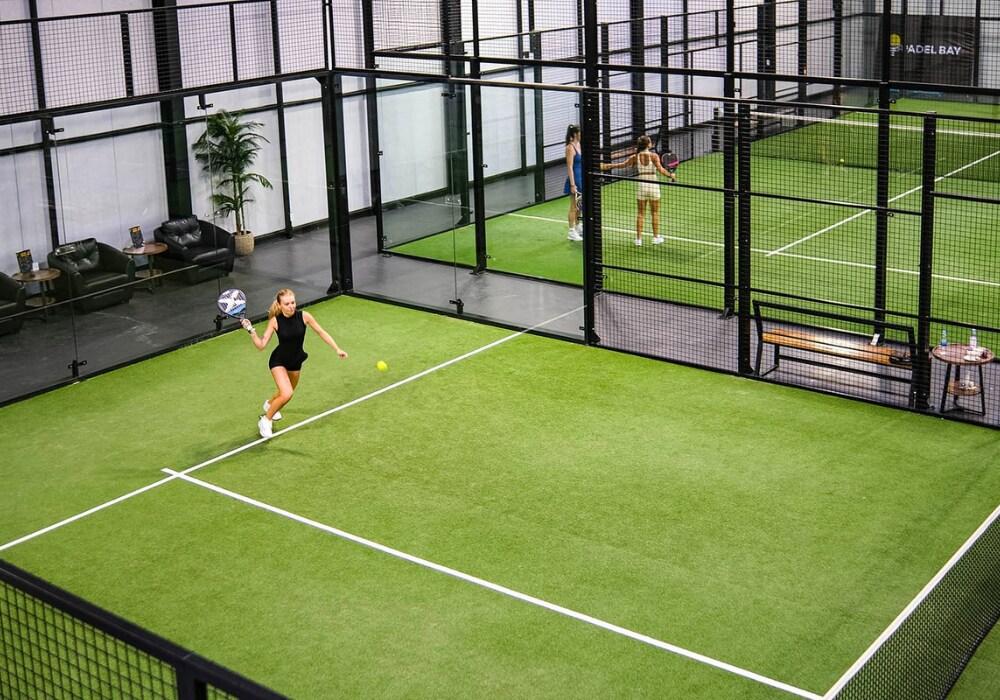 Padel players playing on a bright green indoor padel court at Padel Bay Indoor Club in Phuket, Thailand