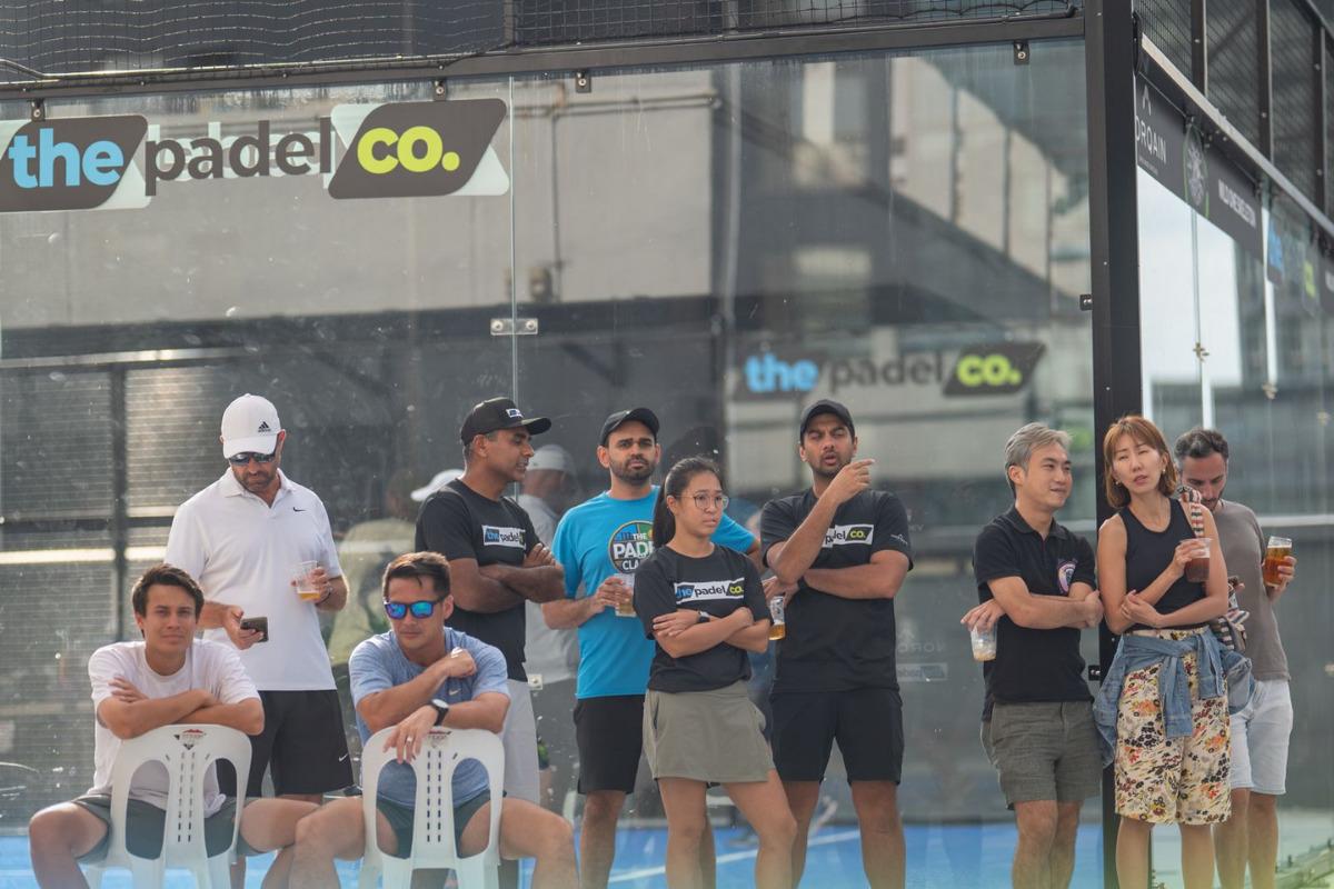 Players and spectators gathered beside the court at The Padel Co in Bugis, Singapore, watching a padel match.