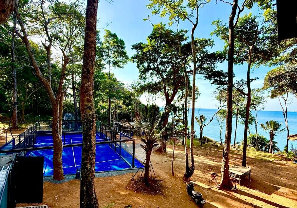 A blue padel court set among trees overlooking the ocean at Padel Lodge in Koh Chang, Thailand