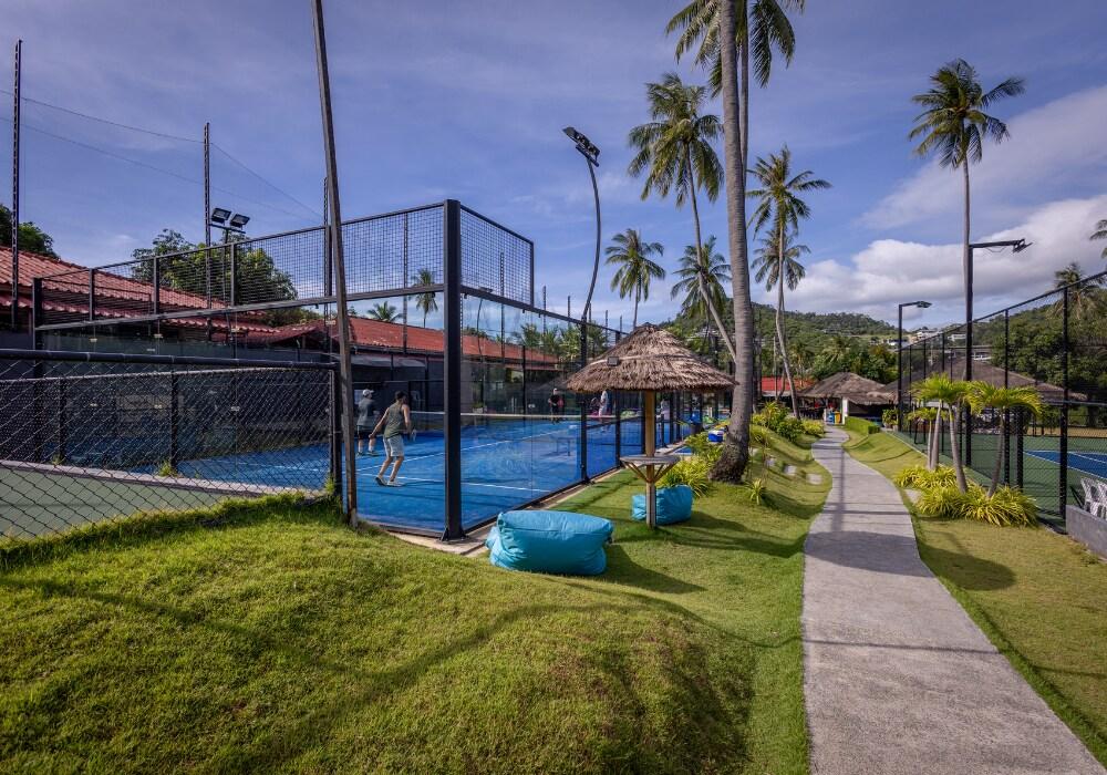 Padel players on a blue outdoor padel court surrounded by palm trees at Padel Samui in Koh Samui, Thailand, under a bright sunny sky