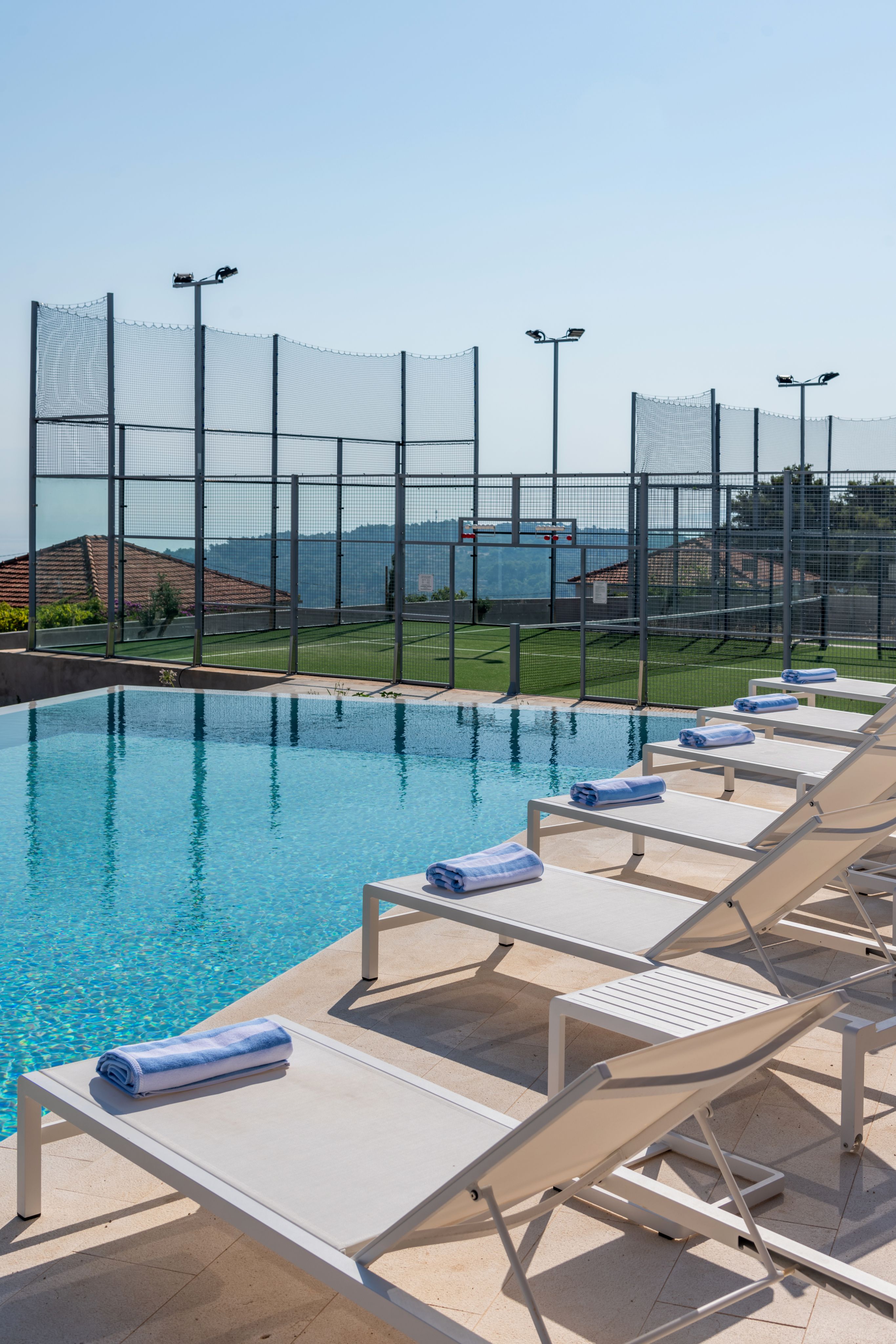 Poolside lounge chairs next to padel courts