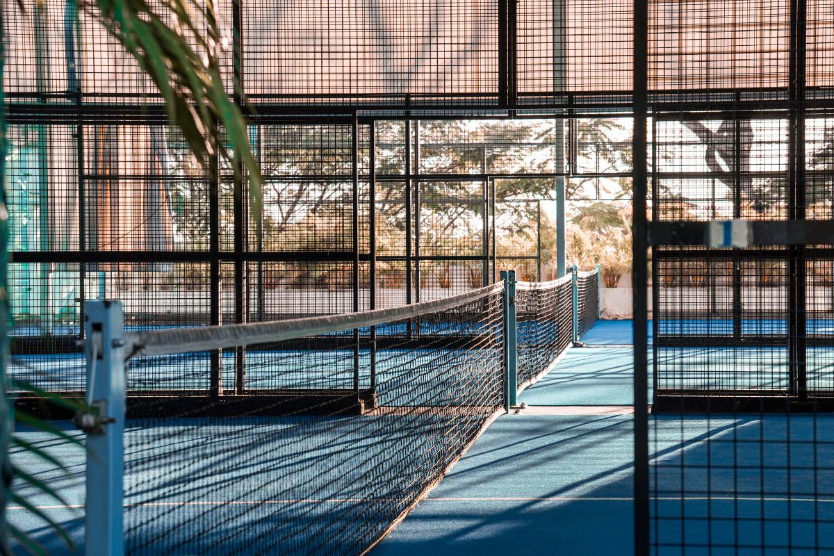 Sunlit blue court at Ricochet Padel Sentosa, with metal cage walls and a net stretching across the center.