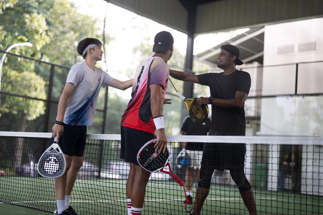 Three padel players standing by the net, wrapping up a game on an indoor court.